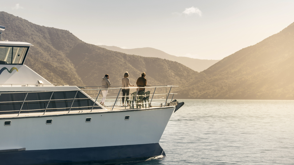 Cruising the Marlborough Sounds at the top of New Zealand's South Island, people view the sun set over the bush clad hills from the bow of MV Odyssea