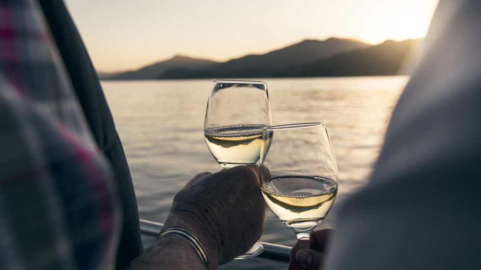 Close up of hands holding wine glasses with the Marlborough Sounds in the background at sunset - the top of New Zealand's South Island