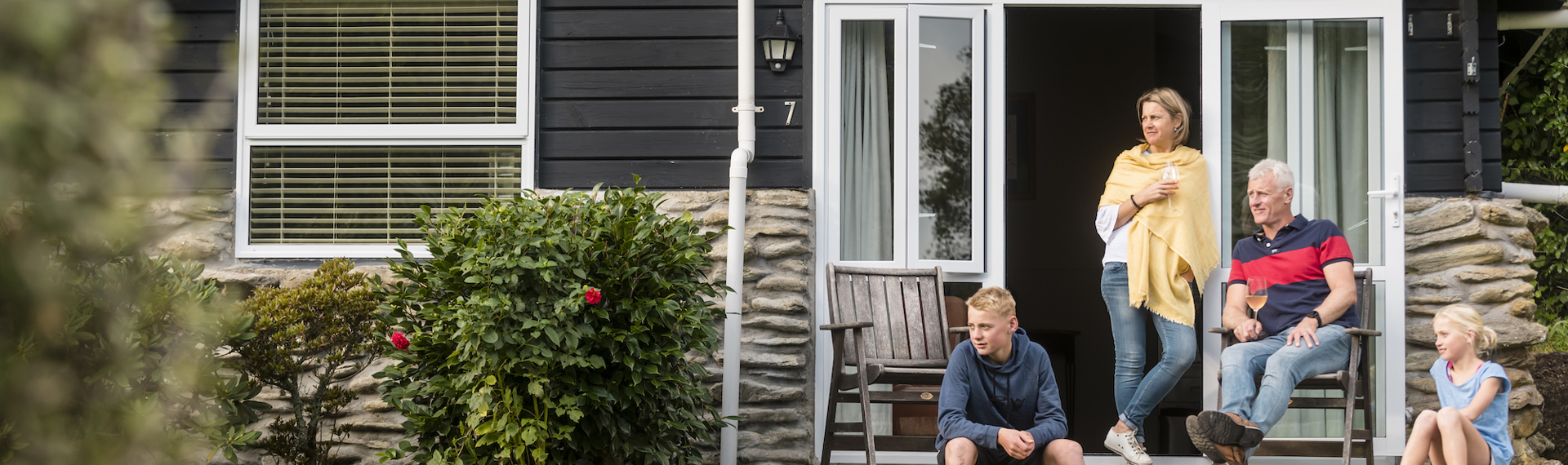 A family of four relax on the private deck of a Cook's Cottage at Furneaux Lodge in the Marlborough Sounds, New Zealand.