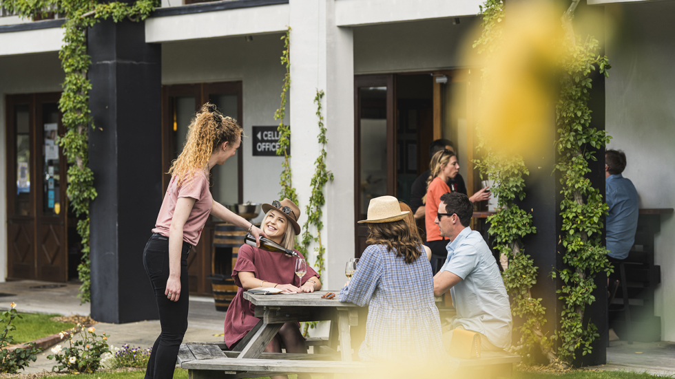 Four people enjoy a guided wine tasting outside at a winery cellar door on a wine tour in Marlborough near Blenheim, at the top of New Zealand's South Island