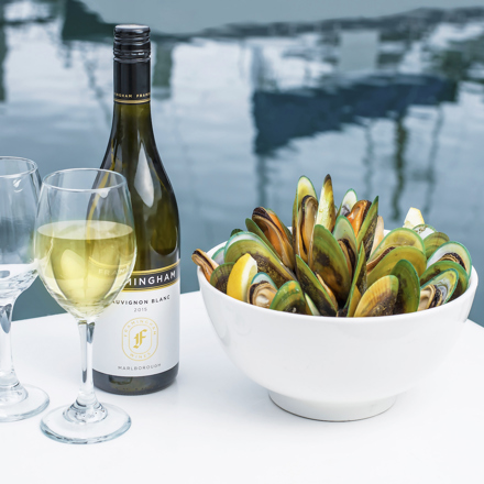 Two glasses of wine, a bottle of wine and bowl of freshly steamed mussels with the Marlborough Sounds in the background, at the top of New Zealand's South Island