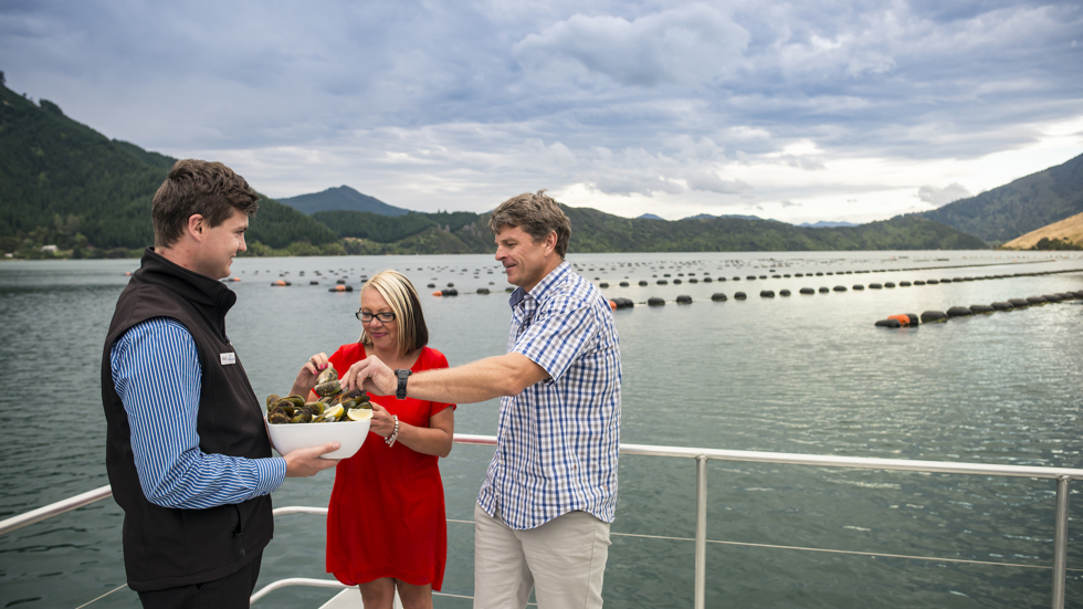 A couple taste steamed fresh Greenshell mussels, served at the source on a Seafood Odyssea cruise in New Zealand's Marlborough Sounds from Picton.