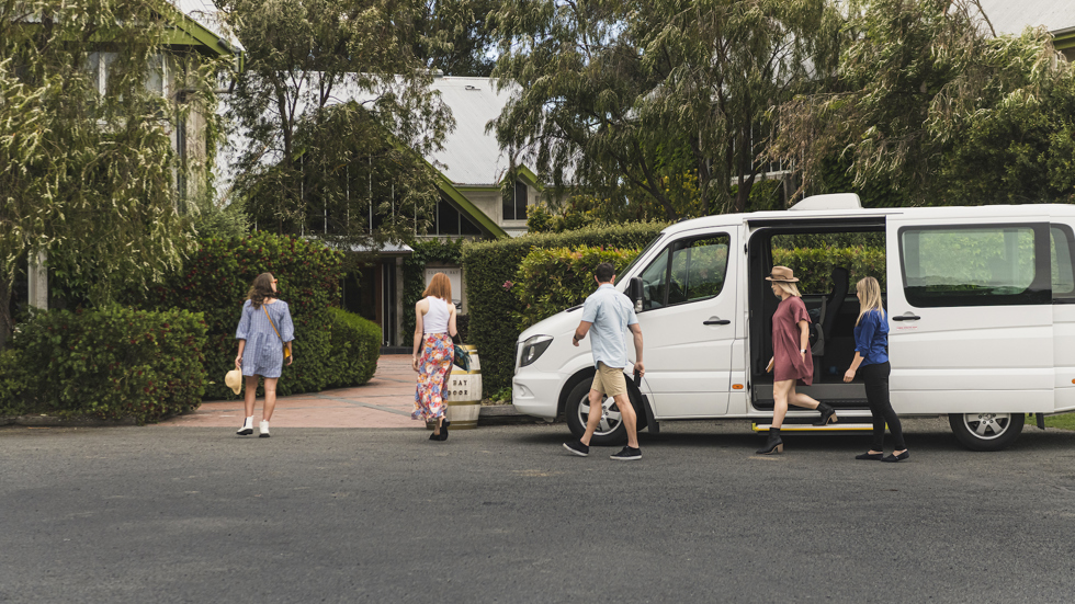 Group of four exiting a van and walking into a winery cellar door on a wine tour in Marlborough, at the top of New Zealand's South Island