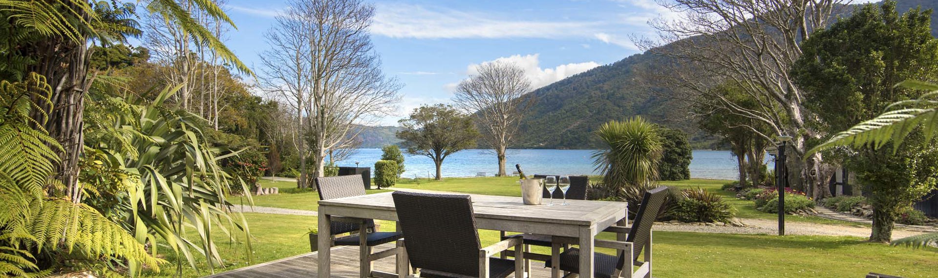 An outdoor dining table on a private Cook's Cottage deck overlooking the Endeavour Inlet Bay at Furneaux Lodge in the Marlborough Sounds at the top of New Zealand's South Island.