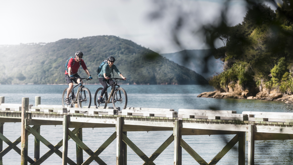 Two mountain bikers on the jetty at Ship Cove/Meretoto, about to start the Queen Charlotte Track in the Marlborough Sounds, New Zealand.