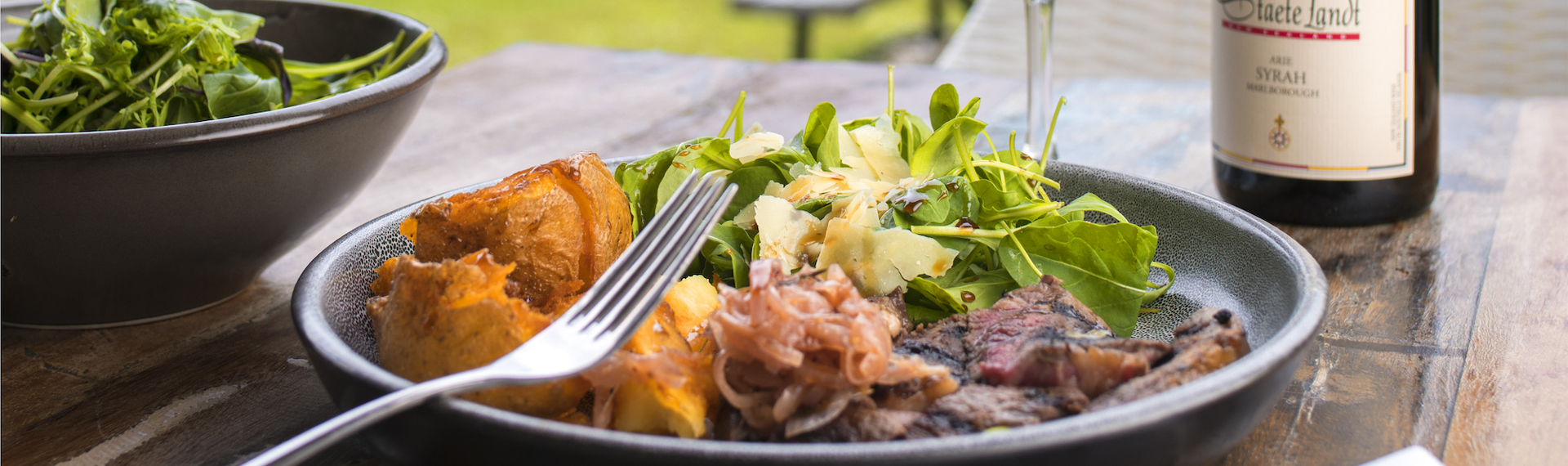 Gourmet steak, potato and salad meal served with ocean view and glass of Staete Landt Syrah at the Furneaux Lodge Restaurant in the Marlborough Sounds at the top of New Zealand's South Island.