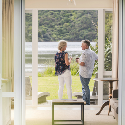 A couple enjoying glasses of Pinot Noir outside on an Endeavour Suite Rows of wine glasses on a shelf at the Furneaux Lodge  in the Marlborough Sounds at the top of New Zealand's South Island.