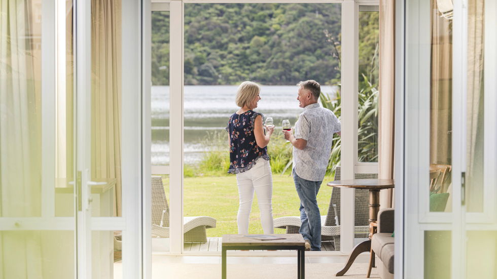 A couple enjoying glasses of Pinot Noir outside on an Endeavour Suite Rows of wine glasses on a shelf at the Furneaux Lodge  in the Marlborough Sounds at the top of New Zealand's South Island.