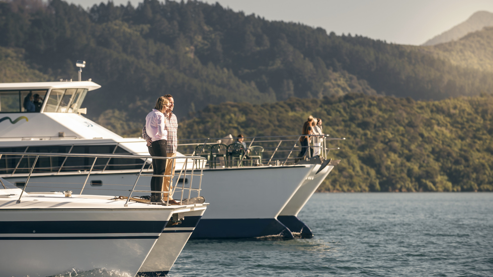 Two launches next to each other with passengers on the bow cruising in the Marlborough Sounds at the top of New Zealand's South Island.,  